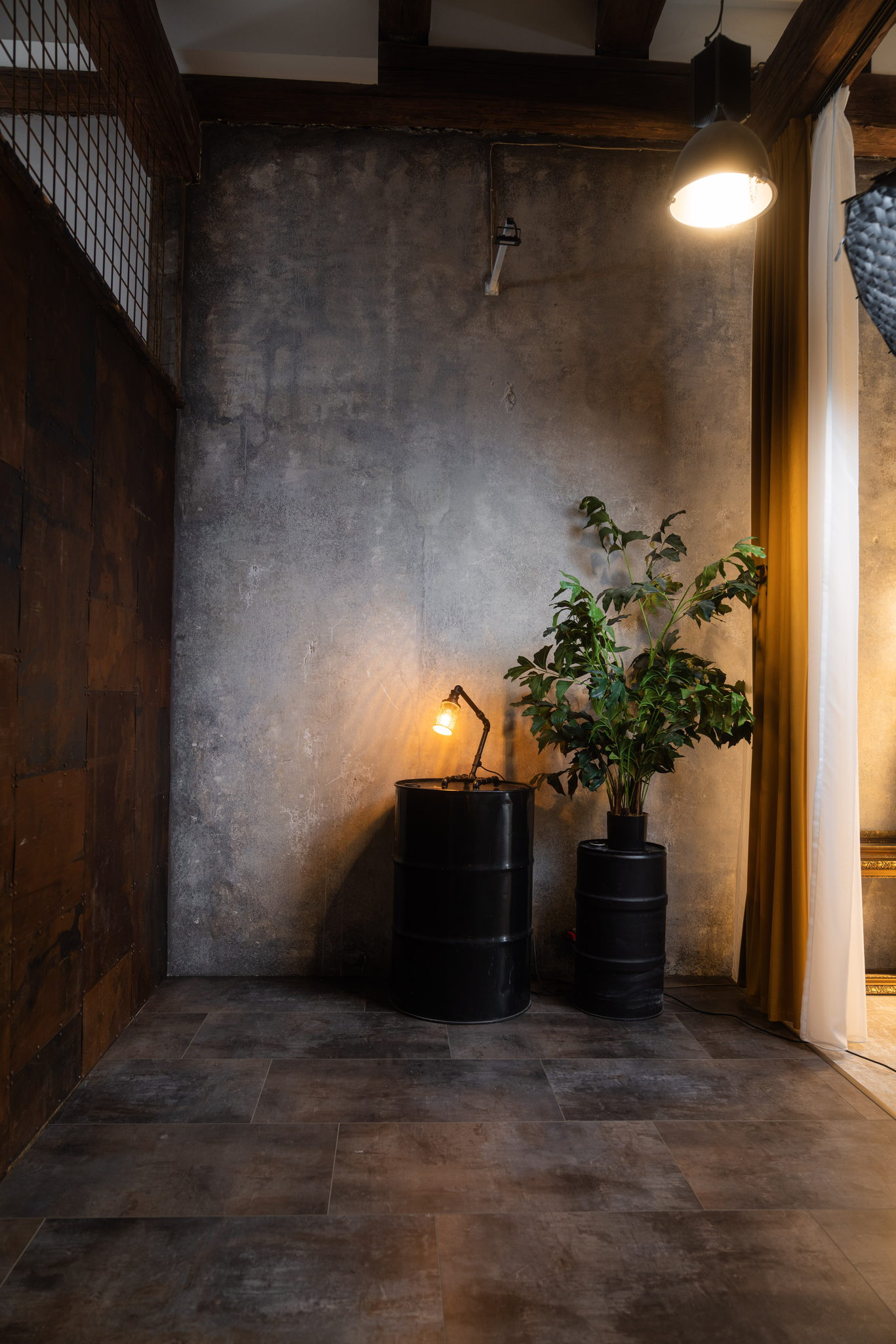 Detail scény Urban Chic — černé sudy, stolní lampa a rostlina u betonové stěny